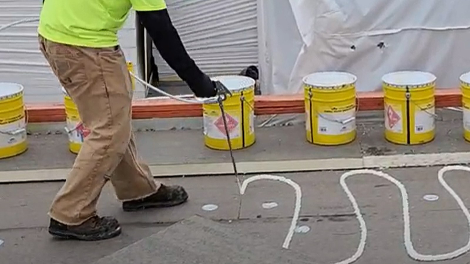 Roofing contractor spraying QDEK adhesive on a commercial flat roof beside staged adhesive canisters.